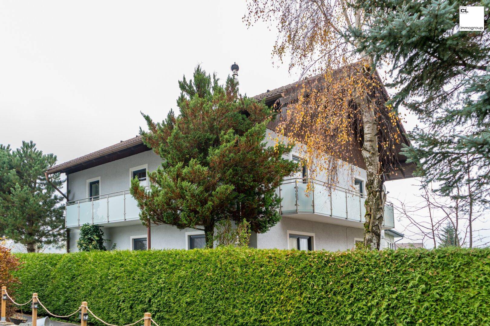 Außenansicht eines Wohnhauses mit mehreren Balkonen und gepflegter Hecke im Vordergrund.