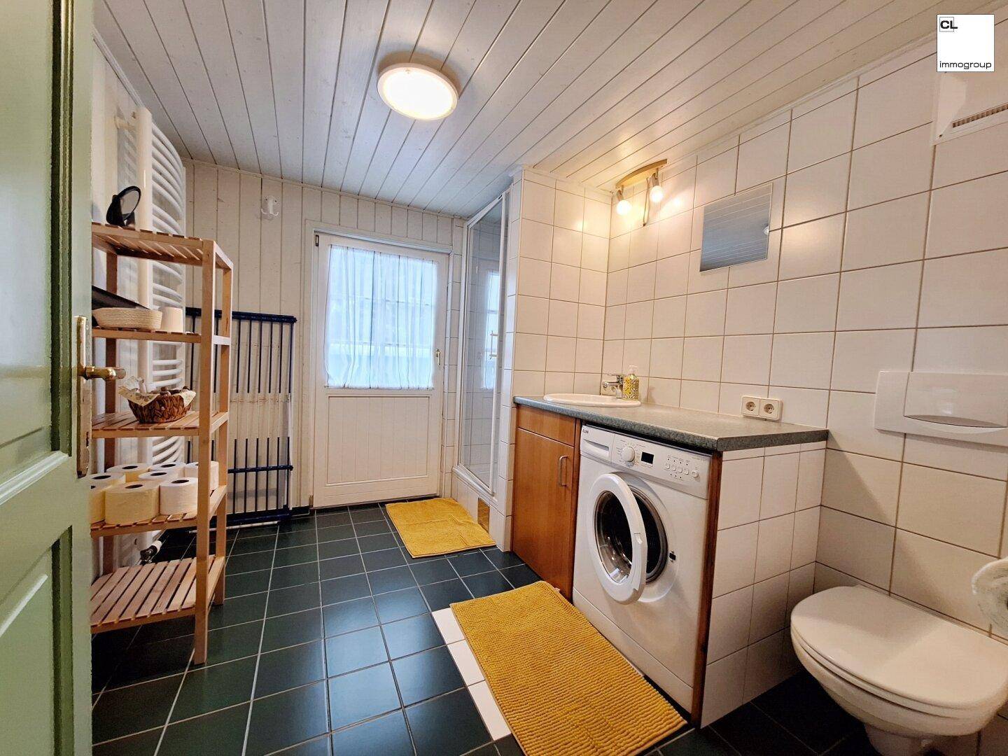 Funktionales Badezimmer mit Dusche, Waschmaschine und weißen Wandfliesen.