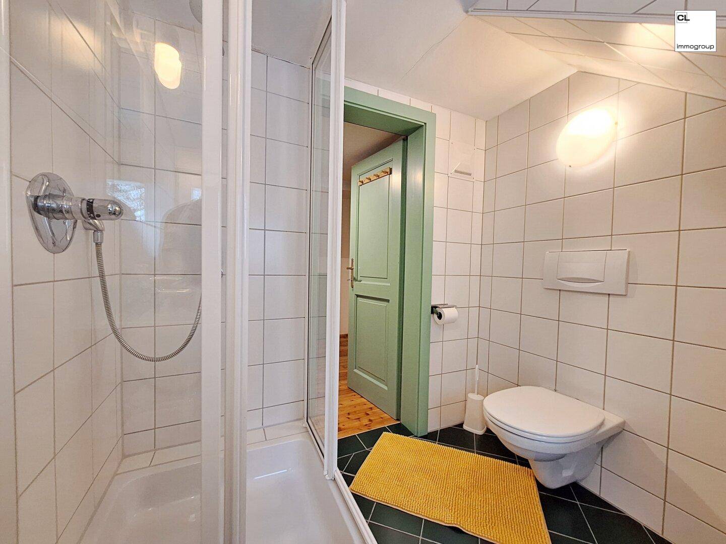 Helles Badezimmer mit Duschkabine, weißen Wandfliesen und dunklem Fliesenboden.