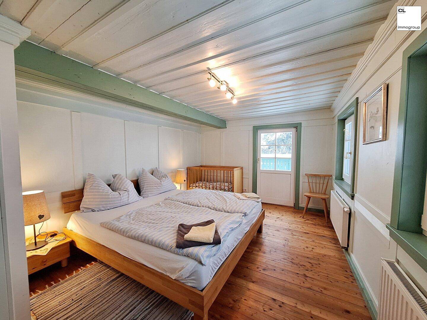 Helles Schlafzimmer mit Doppelbett, Babybett und Holzboden in traditionellem Stil.