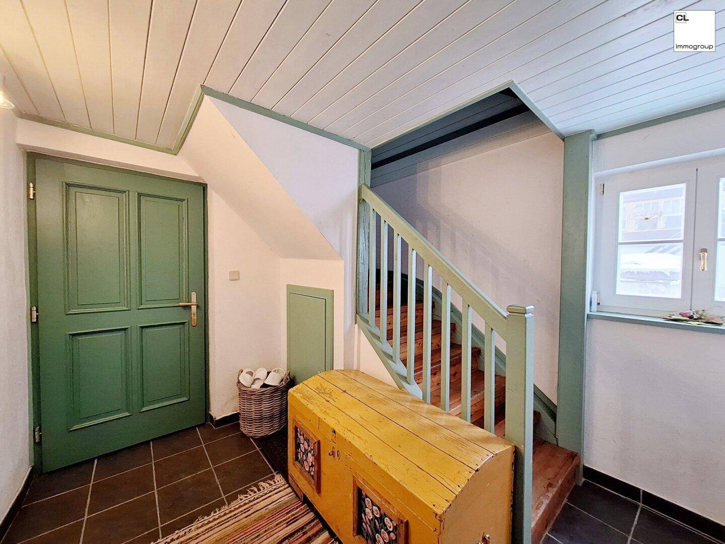 Traditioneller Eingangsbereich mit Holztreppe, dunklen Fliesen und einer rustikalen Holztruhe.