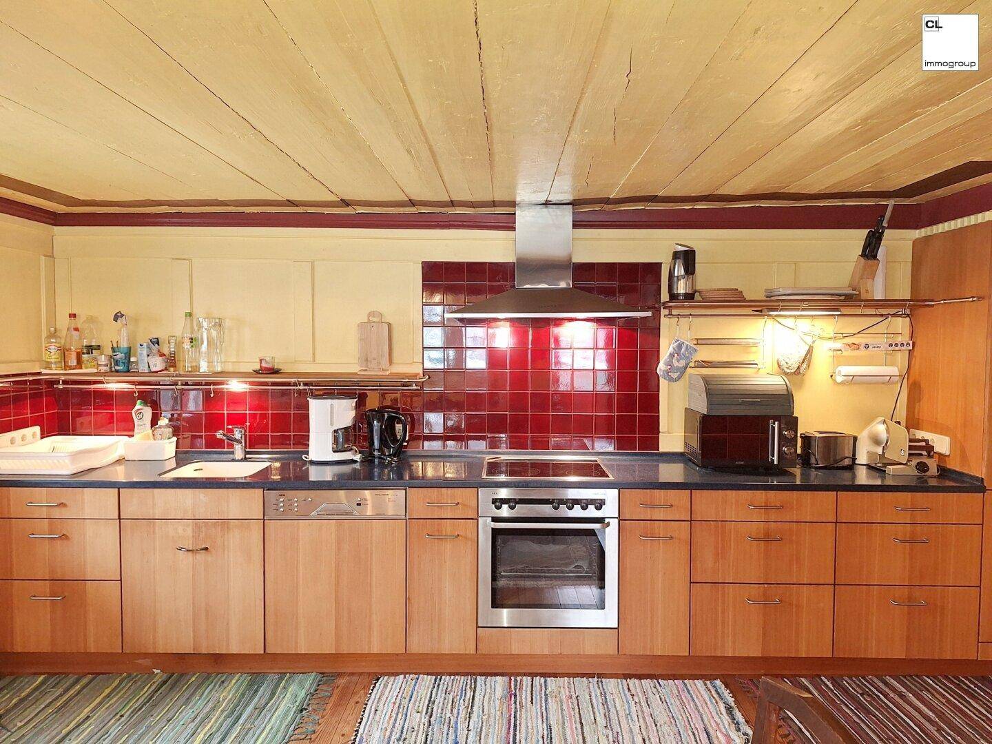 Funktionale Küche mit Holzschränken, roten Fliesen und modernen Edelstahlgeräten.