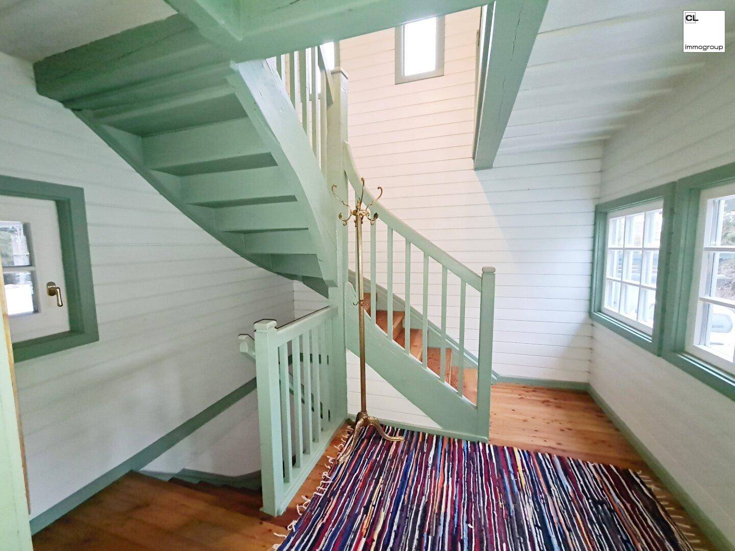 Helle Holztreppe mit grünem Geländer und Holzboden in einem traditionellen Haus.