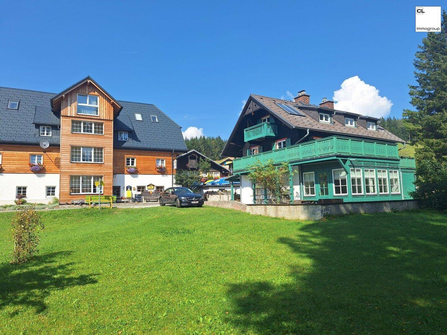 Zwei traditionelle Gebäude mit Holzelementen und einem großen grünen Rasen unter blauem Himmel.
