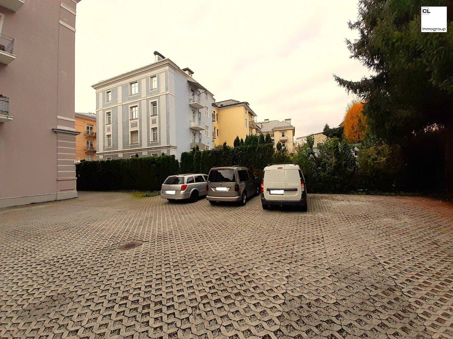 Außenansicht des Gebäudes mit Parkplätzen im Vordergrund und umliegender Bebauung.