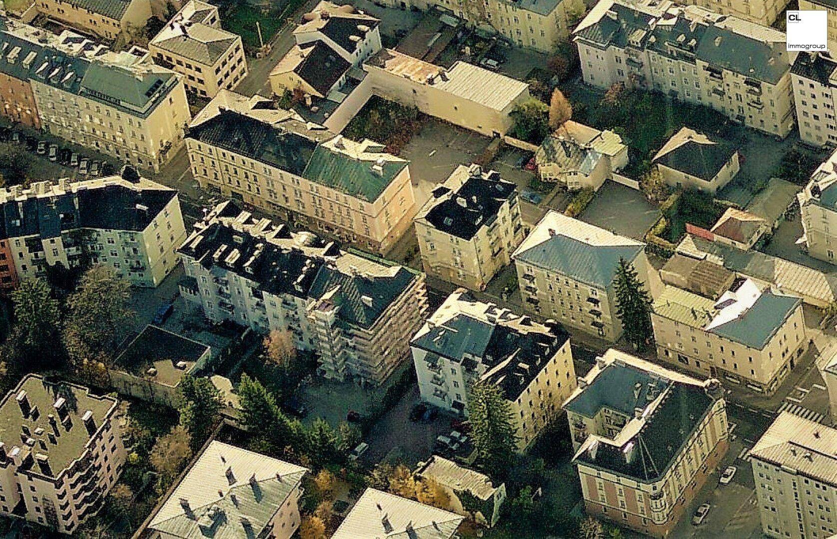 Luftaufnahme einer dicht bebauten Stadtlandschaft mit verschiedenen Gebäuden und Grünflächen.