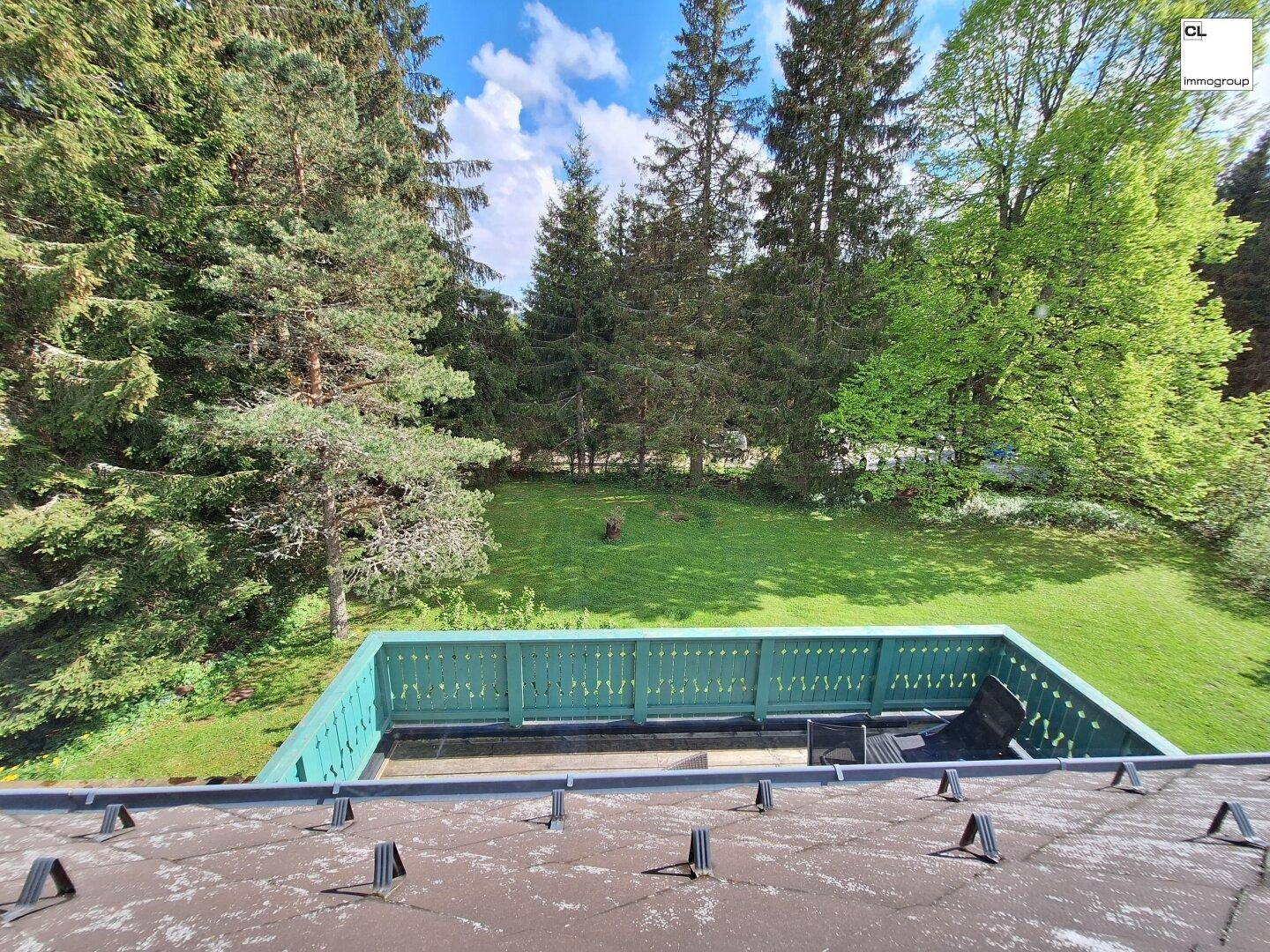 Blick von oben auf eine grüne Gartenfläche mit angrenzendem Balkon und hohen Bäumen.