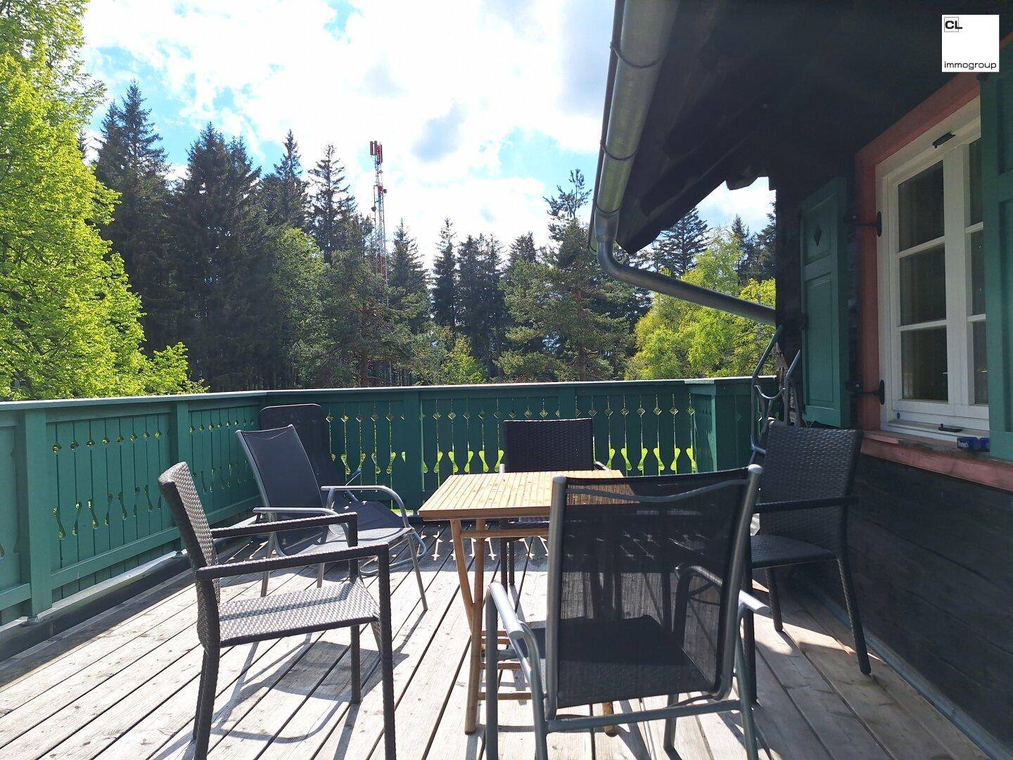 Sonniger Holzbalkon mit grünen Akzenten und Gartenmöbeln, ideal zum Entspannen im Grünen.
