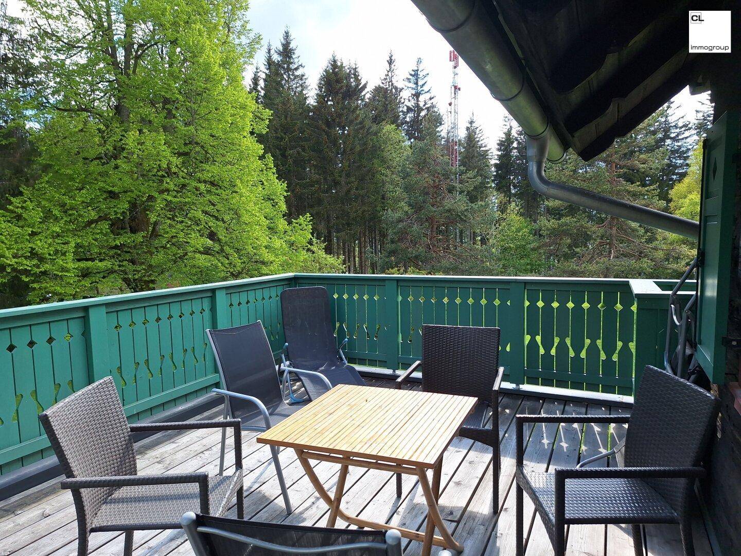 Gemütlicher Holzbalkon mit grünen Geländern und Sitzgelegenheiten, umgeben von Bäumen.