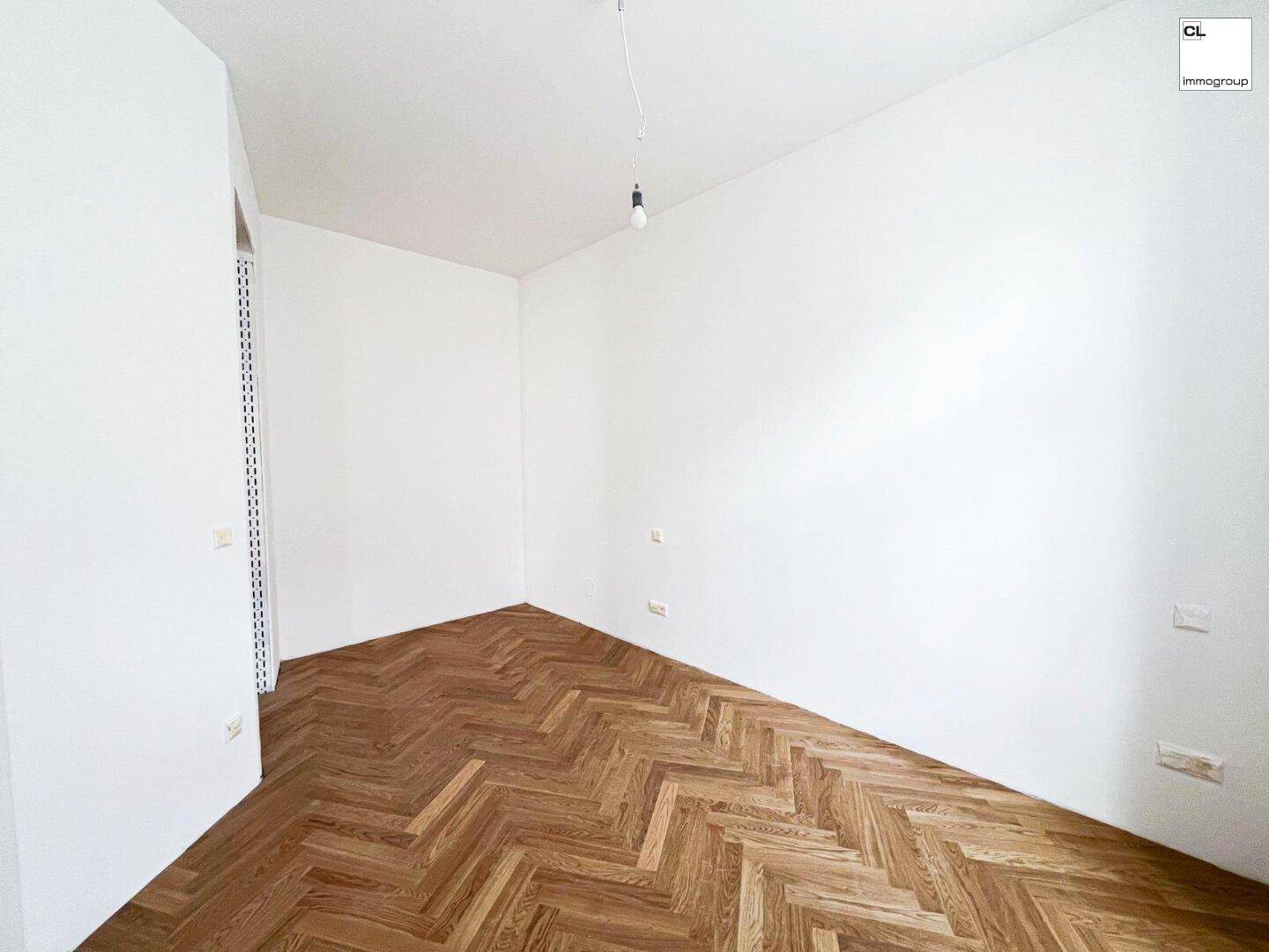 Eckansicht eines leeren Zimmers mit Fischgrätparkett und frisch gestrichenen weißen Wänden.