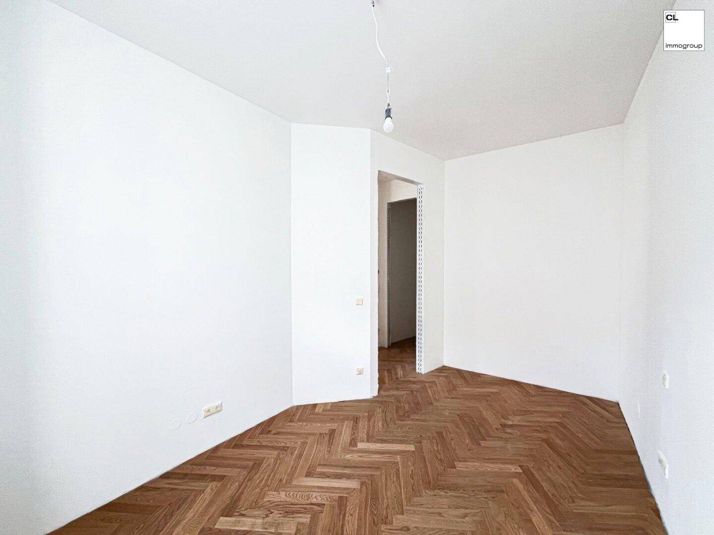 Helles Zimmer mit Fischgrätparkett und offenem Zugang zu einem angrenzenden Bereich.