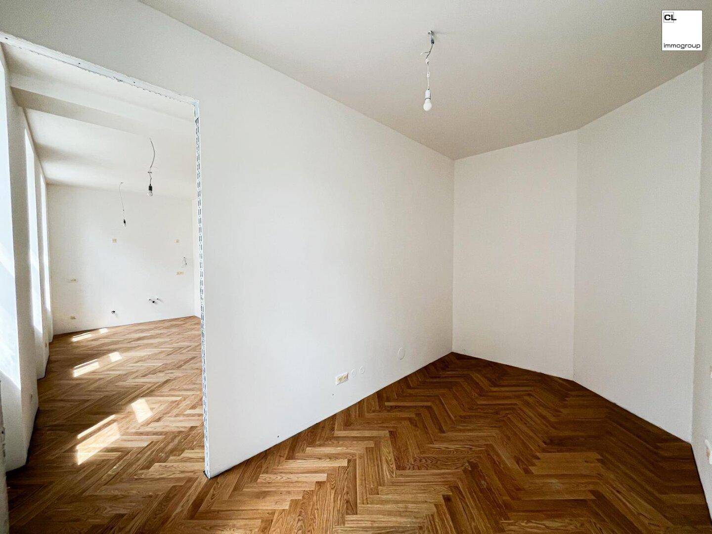 Leeres Zimmer mit Fischgrätparkett und weiß gestrichenen Wänden, bereit zur Einrichtung.