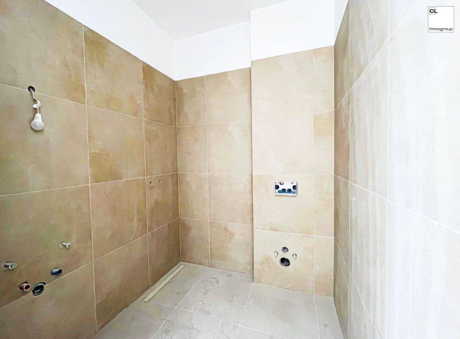 Unfertiges Badezimmer mit beigefarbenen Fliesen an Wänden und Boden, bereit für den Ausbau.