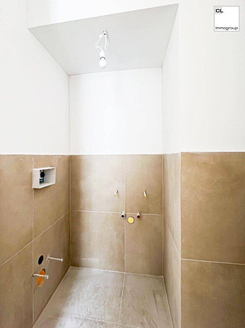 Rohbau eines Badezimmers mit beigefarbenen Fliesen und sichtbaren Sanitäranschlüssen.