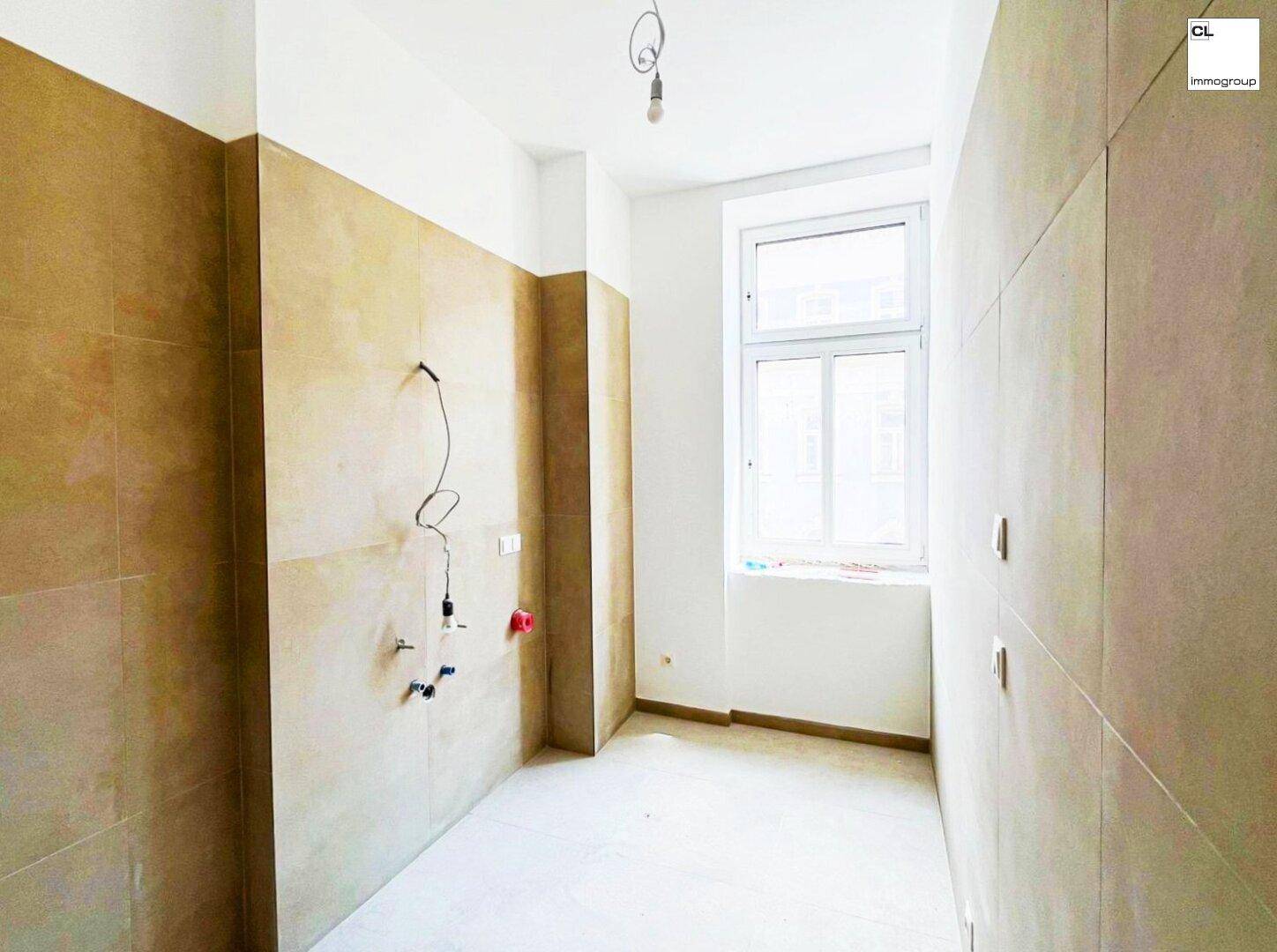 Unfertige Küche mit beigefarbenen Wandfliesen, Fenster und vorbereiteten Anschlüssen.