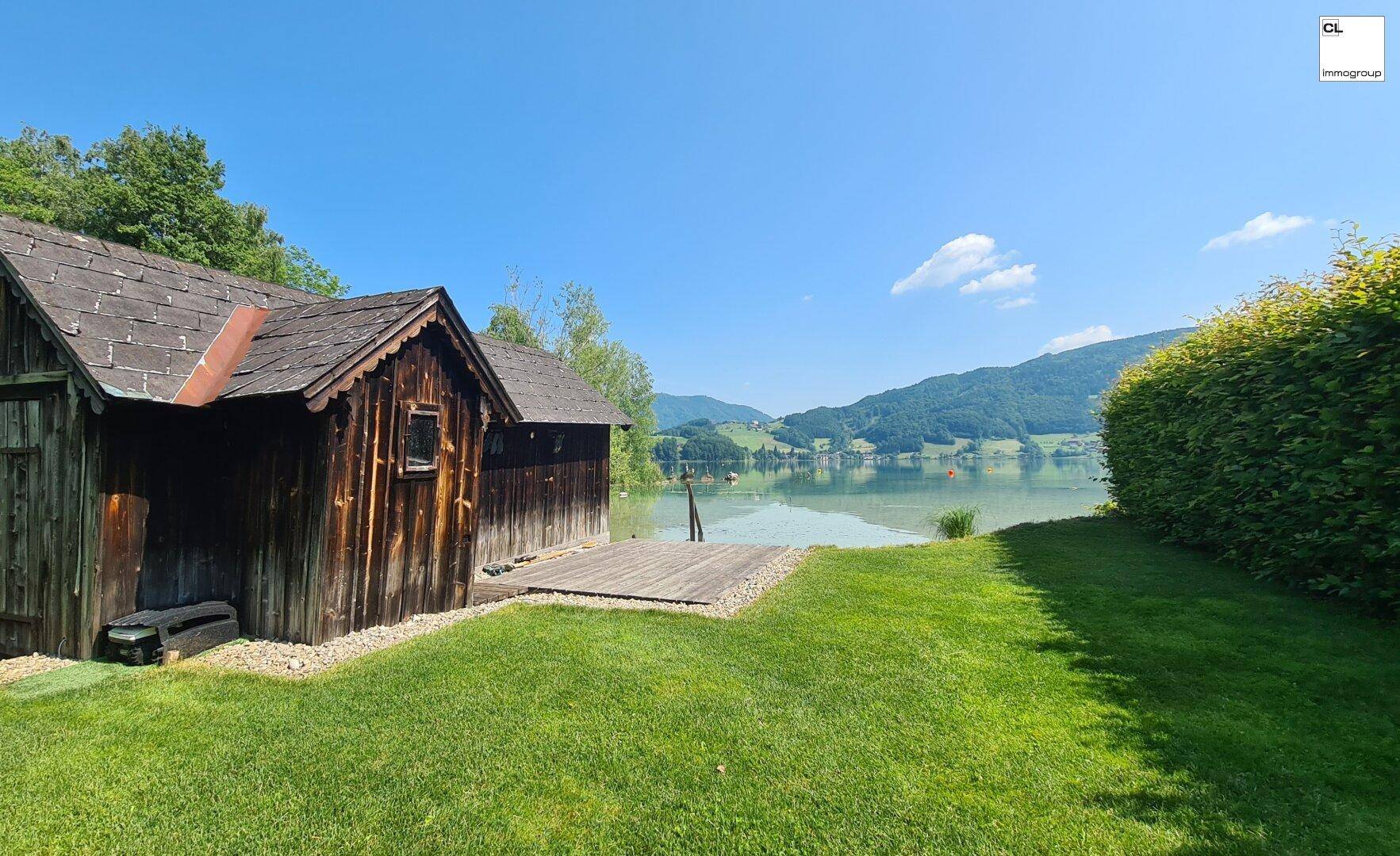 Idyllischer Gartenbereich mit Rasenfläche, direktem Seezugang und rustikalem Bootshaus.