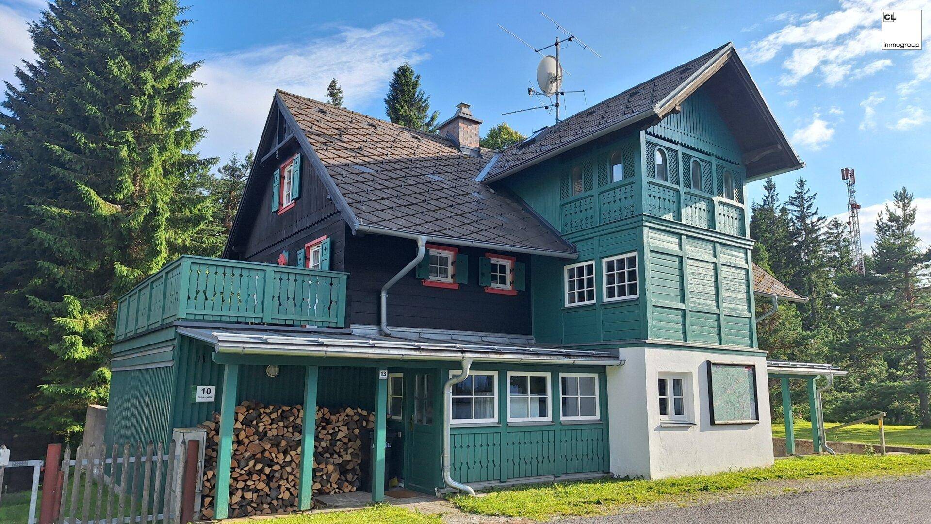 Idyllisches Landhaus mit Holzfassade, grünen Akzenten und einem überdachten Bereich für Holzlagerung.