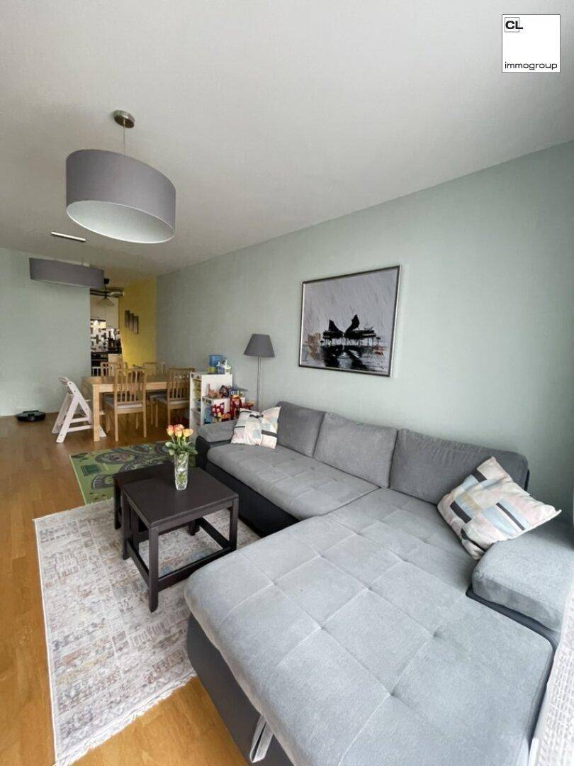 Geräumiger Wohn- und Essbereich mit bequemer grauer Couch und hellem Holzboden.