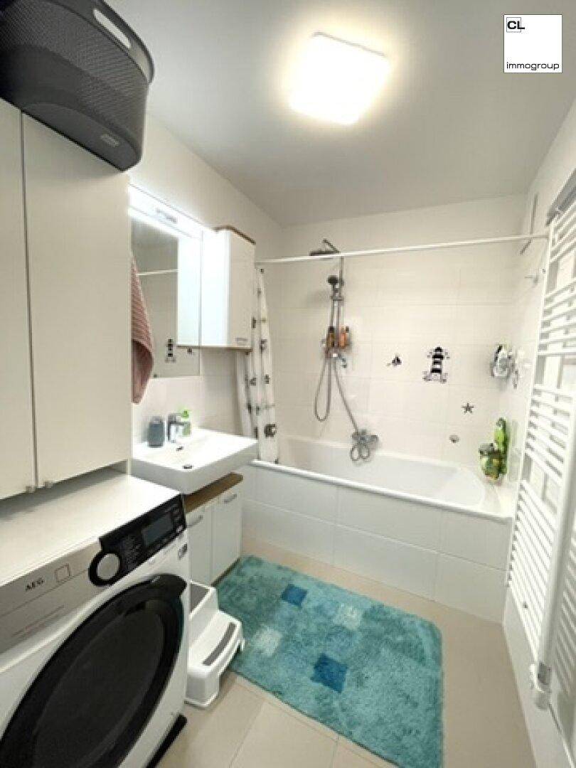 Helles Badezimmer mit Badewanne, Waschmaschine und beheiztem Handtuchhalter für Komfort.