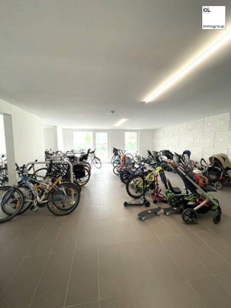 Großer Fahrradraum mit zahlreichen Fahrrädern und Kinderwagen, gut beleuchtet.