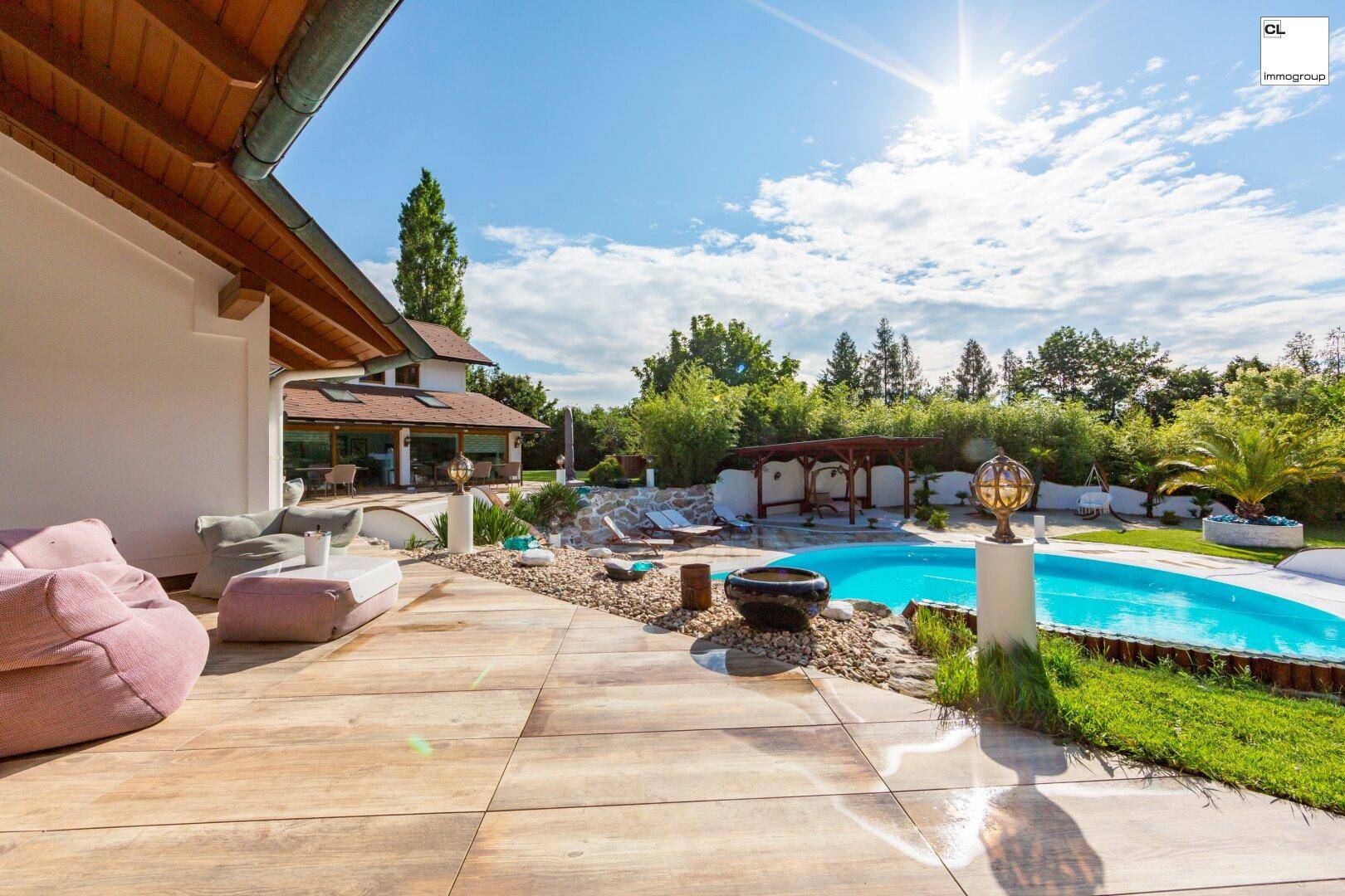 Sonniger Außenbereich mit Terrasse, Pool und bequemen Sitzgelegenheiten im Grünen.