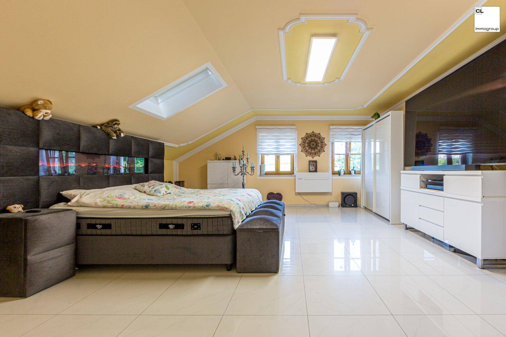 Geräumiges Schlafzimmer mit großem Bett, Dachfenstern und hellen Fliesen unter Dachschrägen.