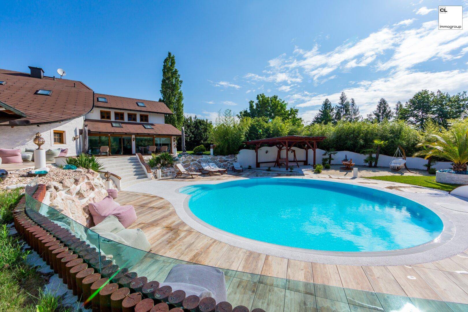 Weitläufiger Außenbereich mit großem Pool, Terrasse und Blick auf die grüne Umgebung.