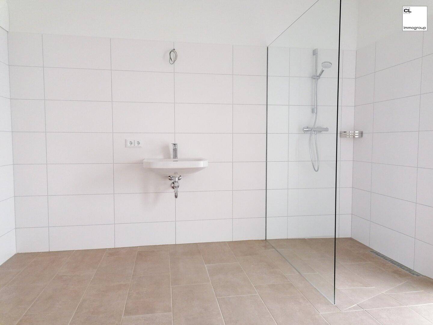 Modernes Badezimmer mit ebenerdiger Dusche, weißen Fliesen und Einzelwaschbecken.