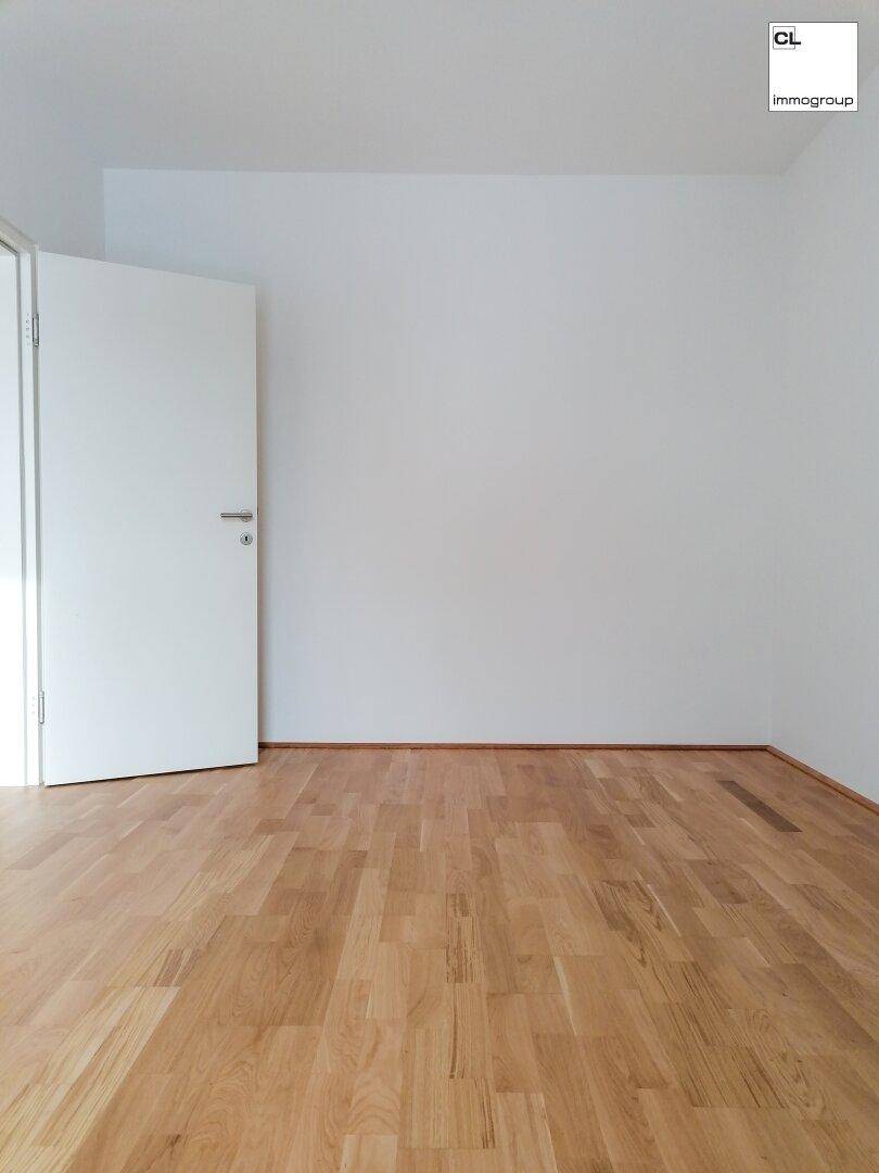 Leeres Zimmer mit hellem Laminatboden und weiß gestrichenen Wänden, ideal als Schlafzimmer.