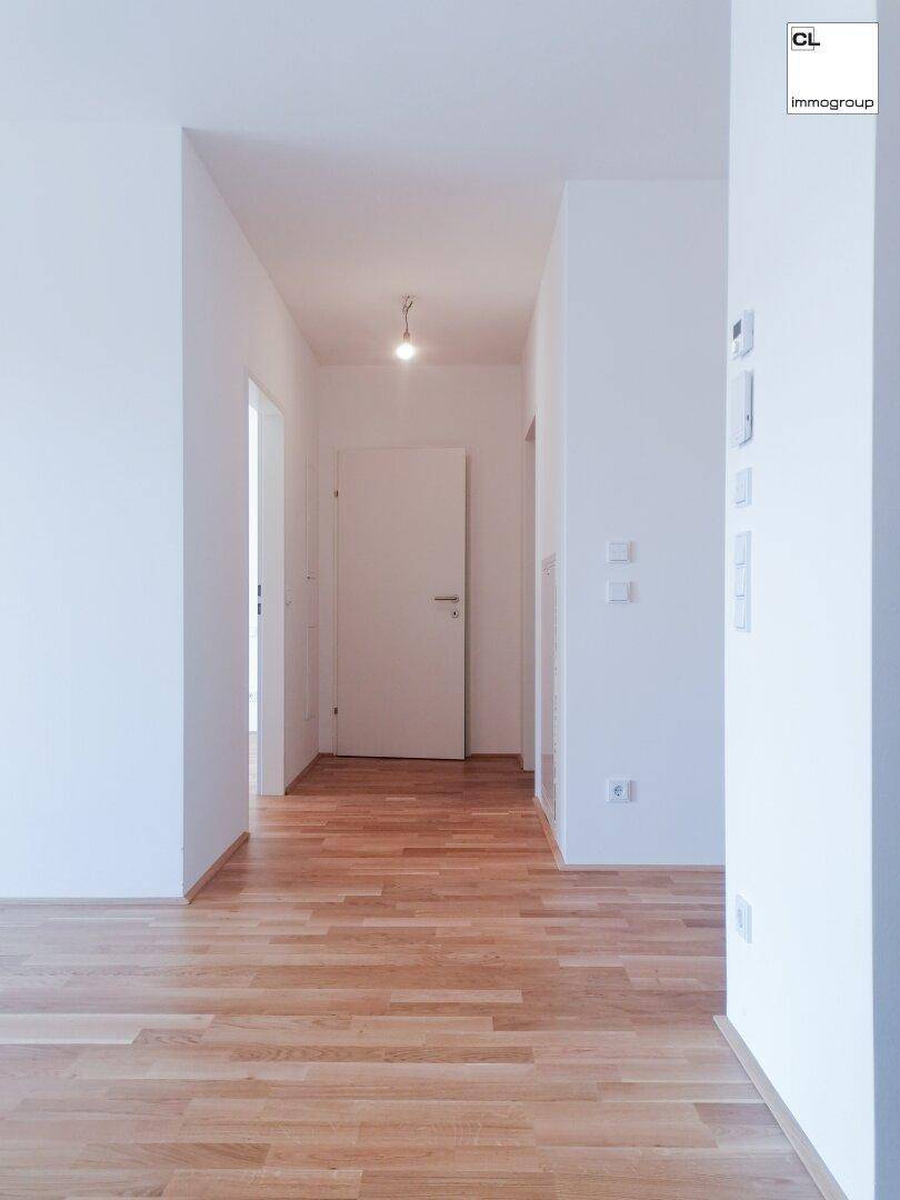 Lichtdurchfluteter Flur mit hellem Parkettboden und weißen Wänden, der zu weiteren Räumen führt.