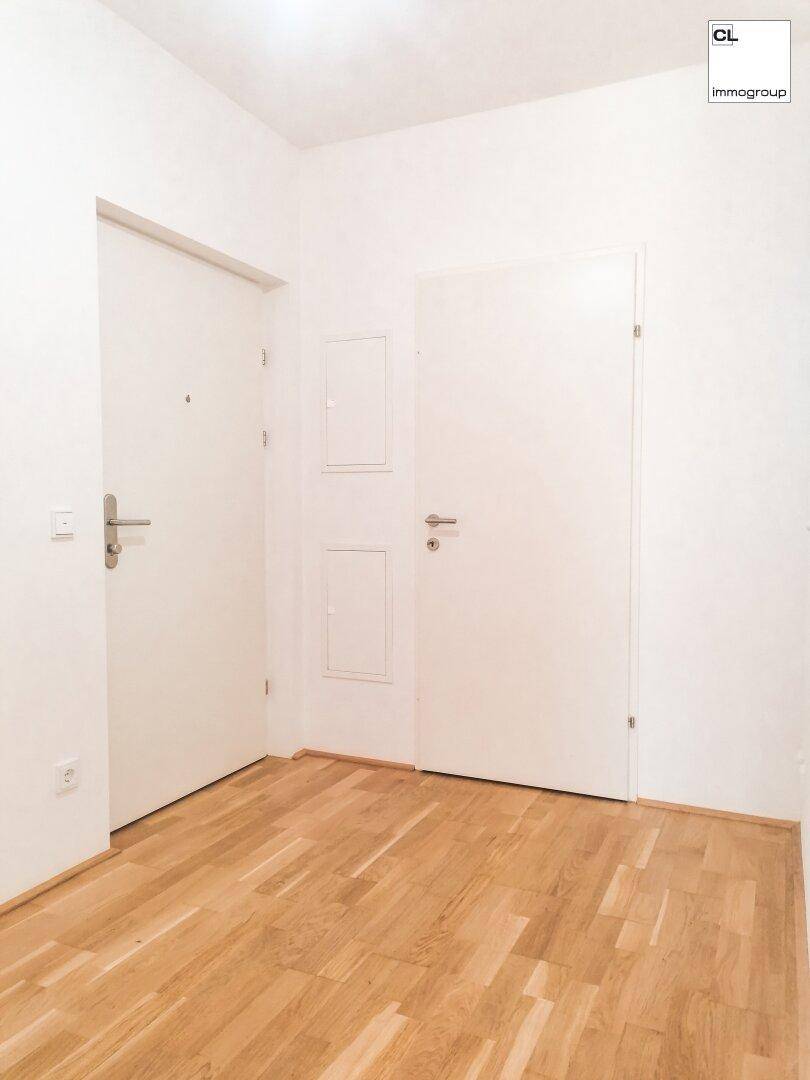 Schlichter Flur mit zwei weißen Türen und hellem Holzboden, der zu weiteren Räumen führt.