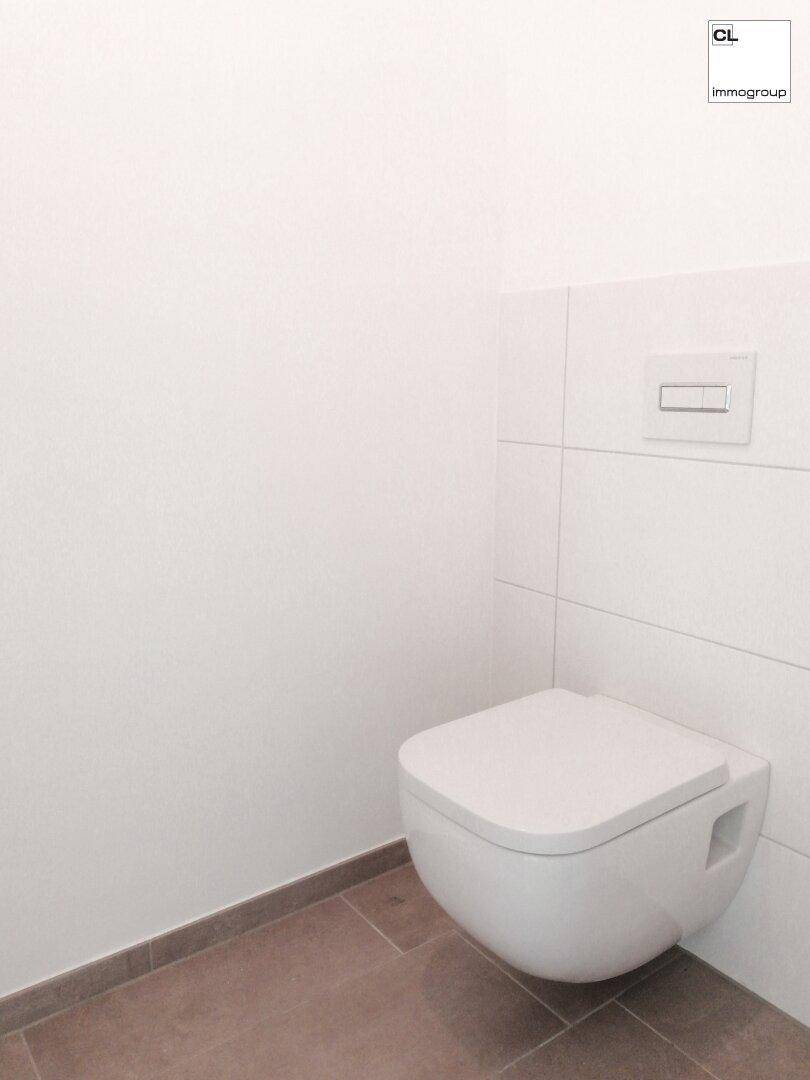 Modernes wandhängendes WC mit weißer Fliesenwand und braunem Boden, sehr sauber und funktional.