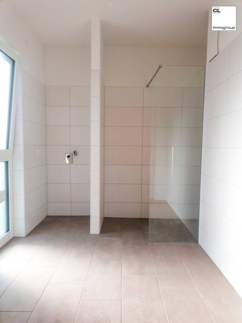 Modernes Badezimmer mit bodengleicher Dusche, weißen Fliesen und Fenster für natürliches Licht.