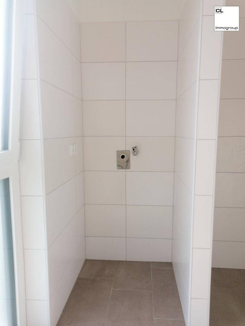 Leere Duschkabine mit weißen Fliesen und Anschluss für Duscharmatur, bereit zur Installation.