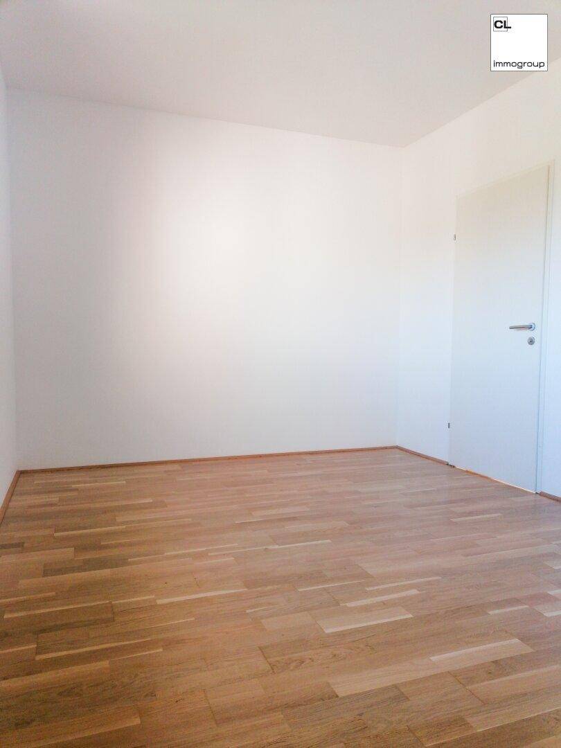Leeres Zimmer mit hellem Holzboden und weißer Tür, bietet vielseitige Nutzungsmöglichkeiten.