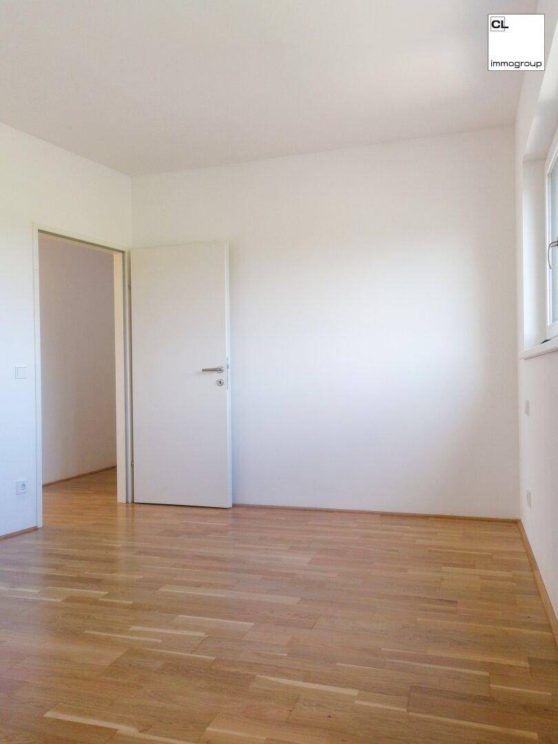 Helles, leeres Zimmer mit Holzboden, Fenster und weißer Tür, ideal für Schlaf- oder Arbeitszimmer.