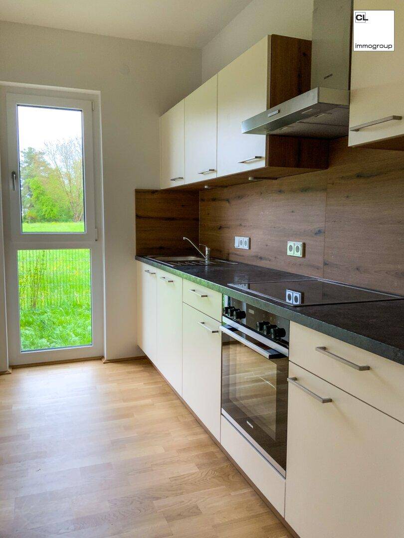 Helle Küche mit weißen Schränken, dunkler Arbeitsplatte und Fenster mit Grünblick.