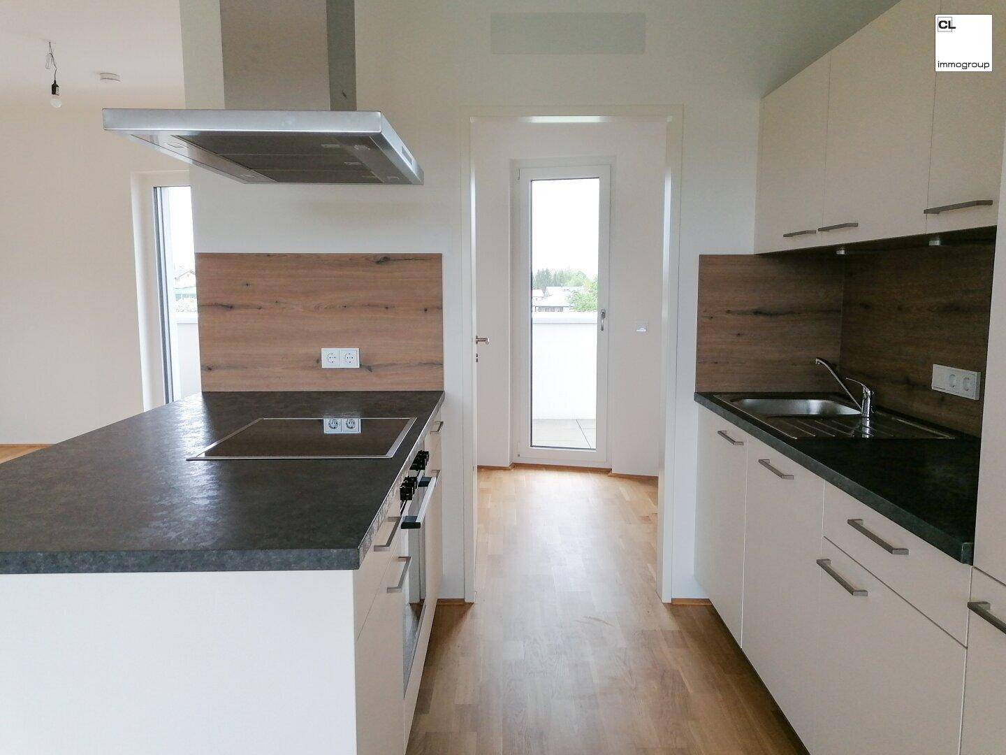 Moderne Einbauküche mit Kochinsel, dunkler Arbeitsplatte und Zugang zum Balkon.