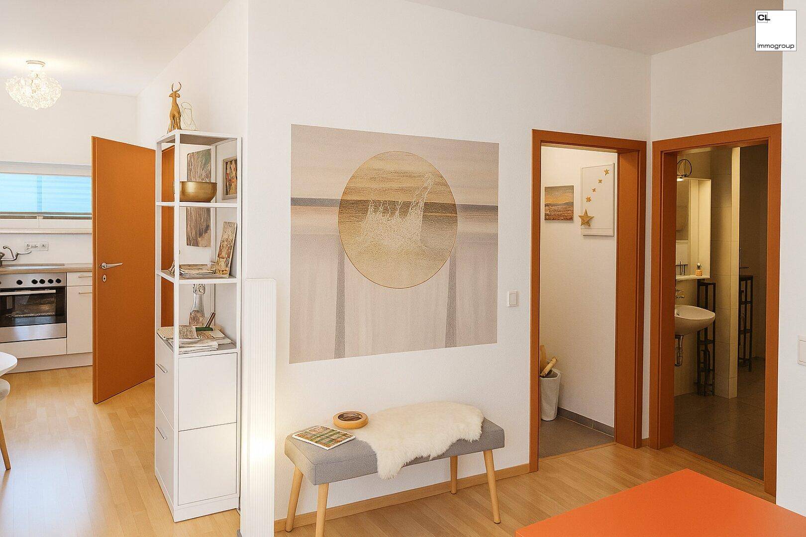 Heller Flur mit Holzboden, Kunst an der Wand und Blick in Küche und Bad.