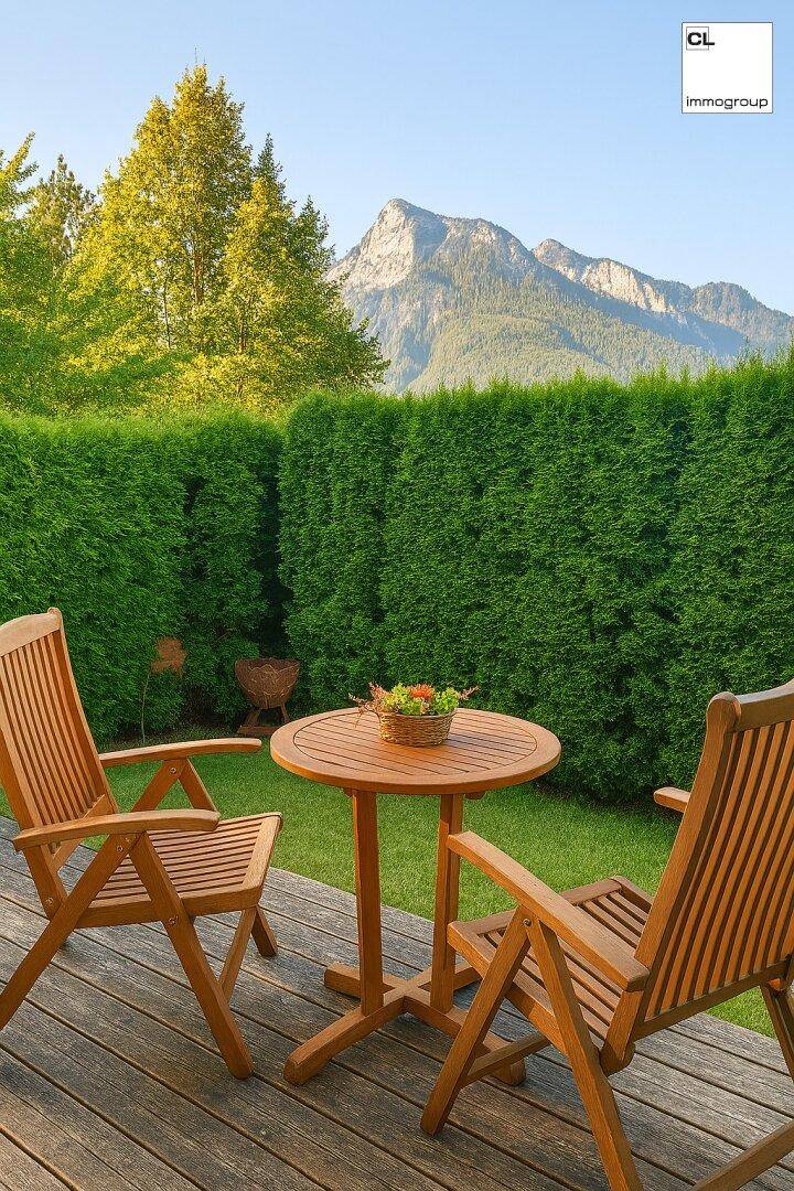 Gemütliche Holzterrasse mit Gartenmöbeln, umgeben von einer Hecke und mit Bergblick.