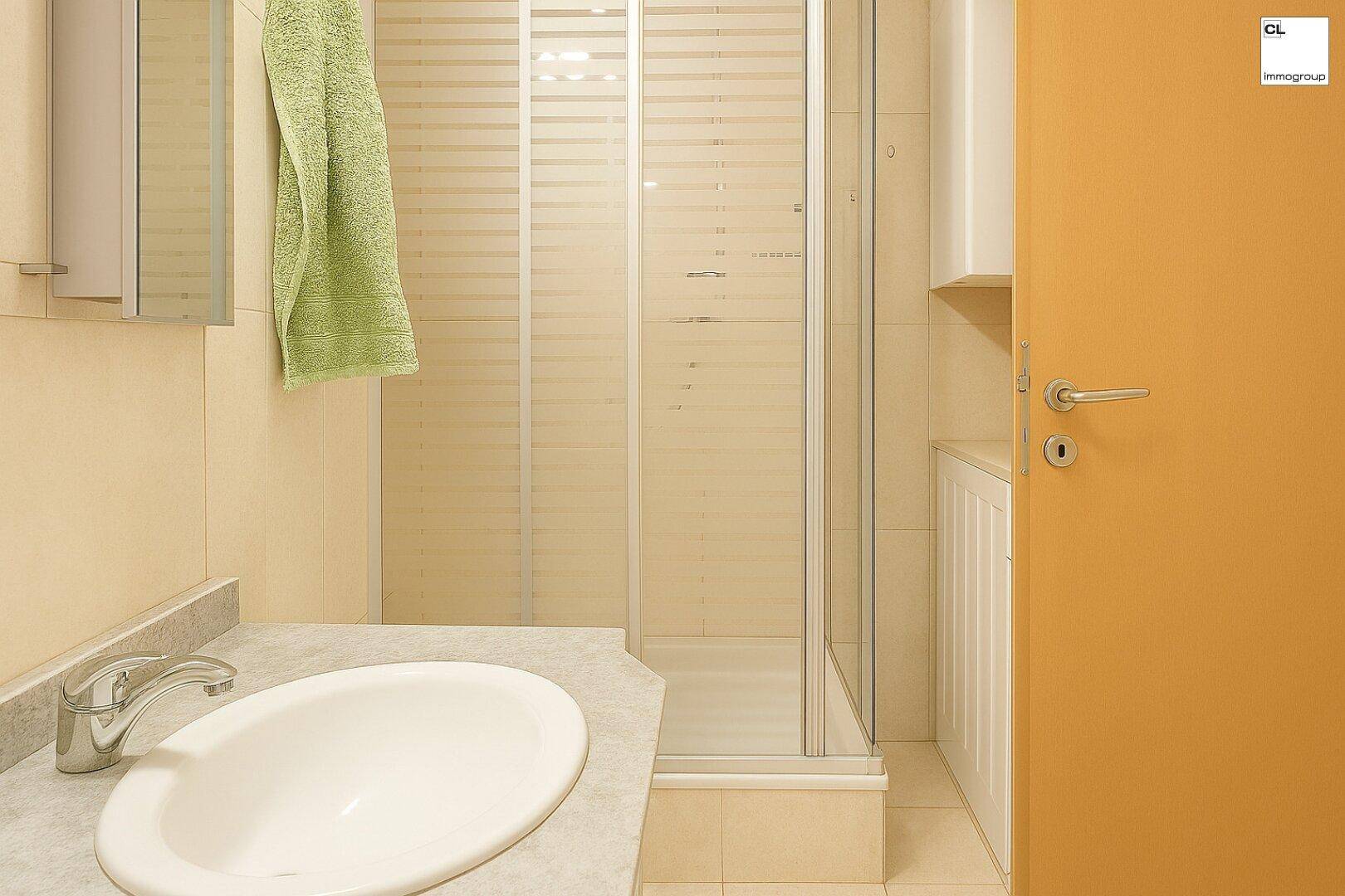 Helles Badezimmer mit Duschkabine, Waschbecken und beigen Fliesen.