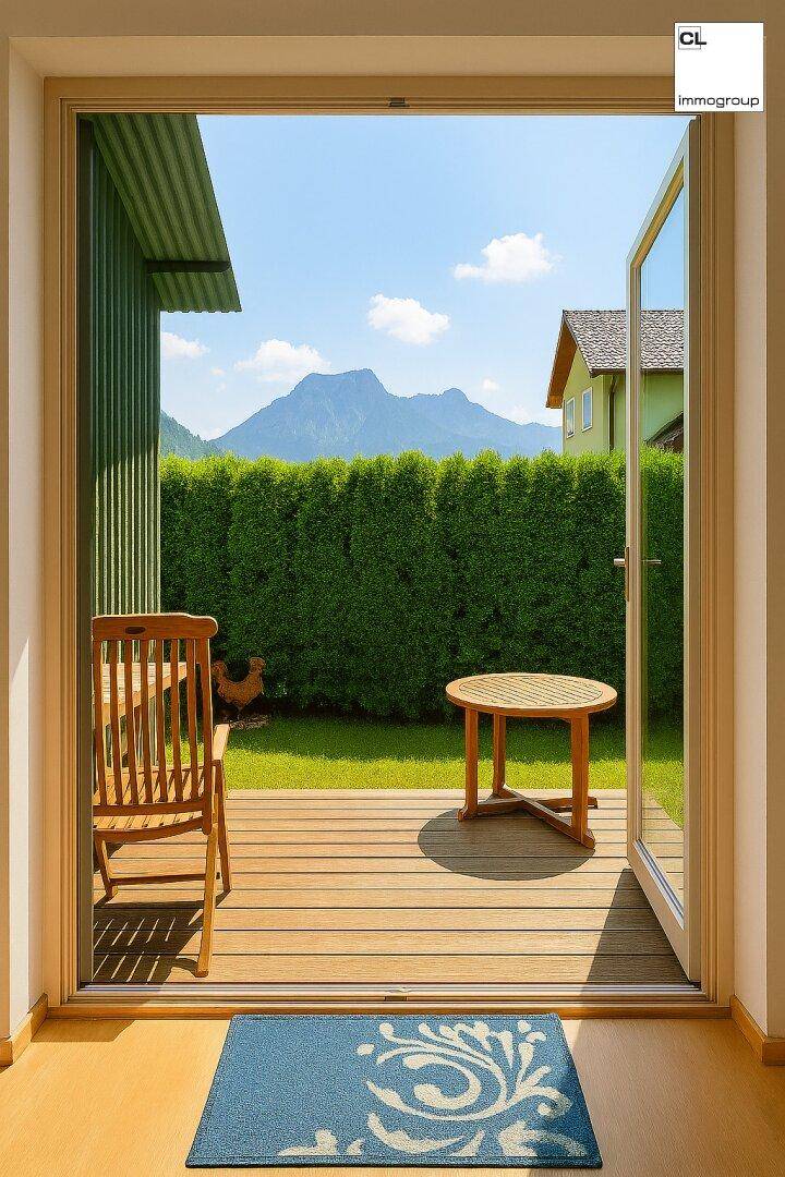 Blick aus einem Raum auf eine Holzterrasse mit Garten und Bergblick.