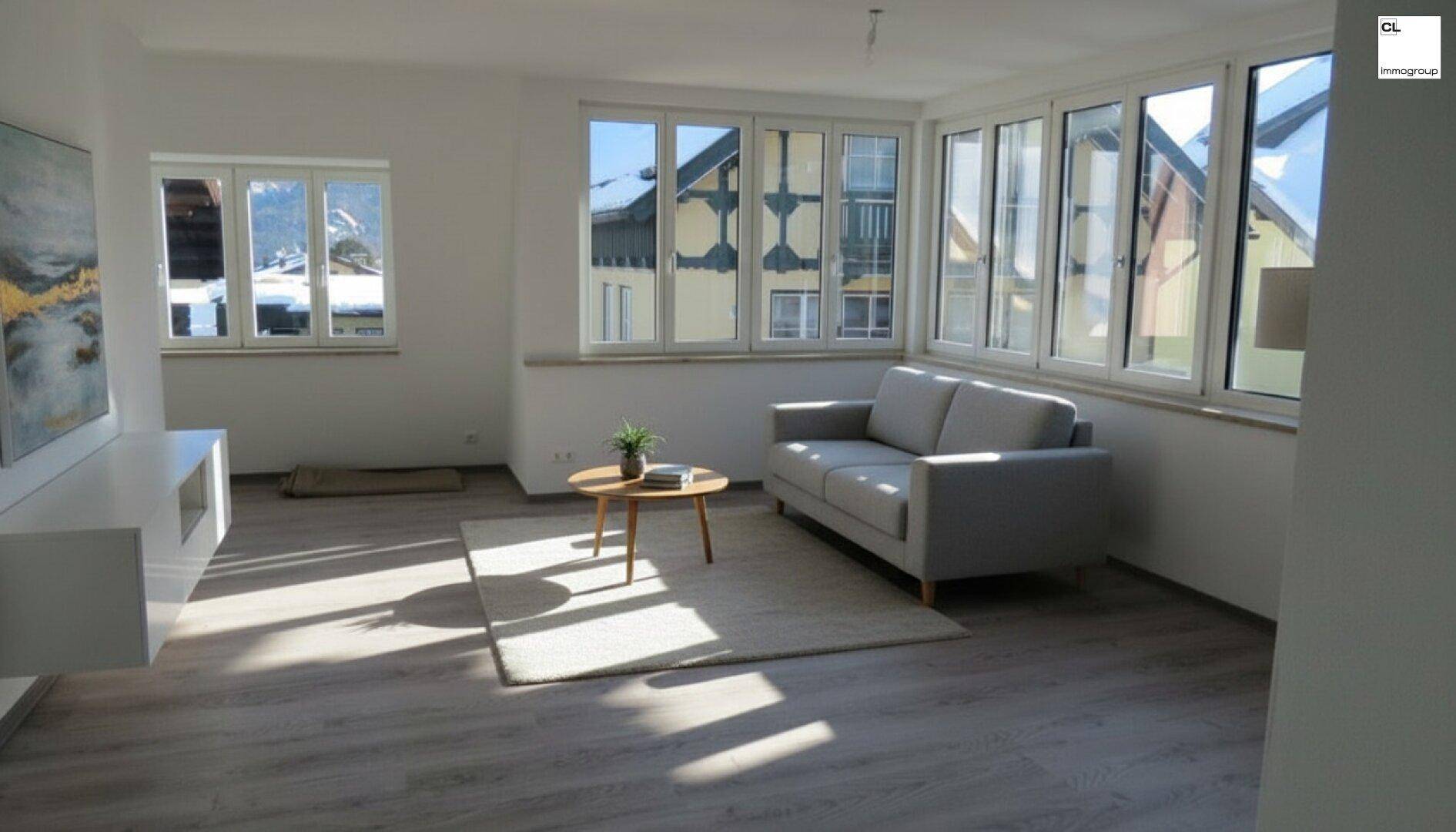 Helles Wohnzimmer mit vielen Fenstern, hellem Boden und minimalistischer Möblierung.