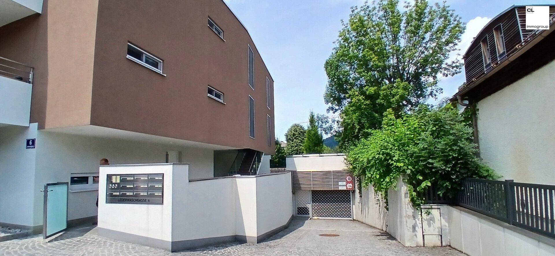 Moderne Wohnanlage mit brauner Fassade und Zufahrt zur Tiefgarage, umgeben von Grün.