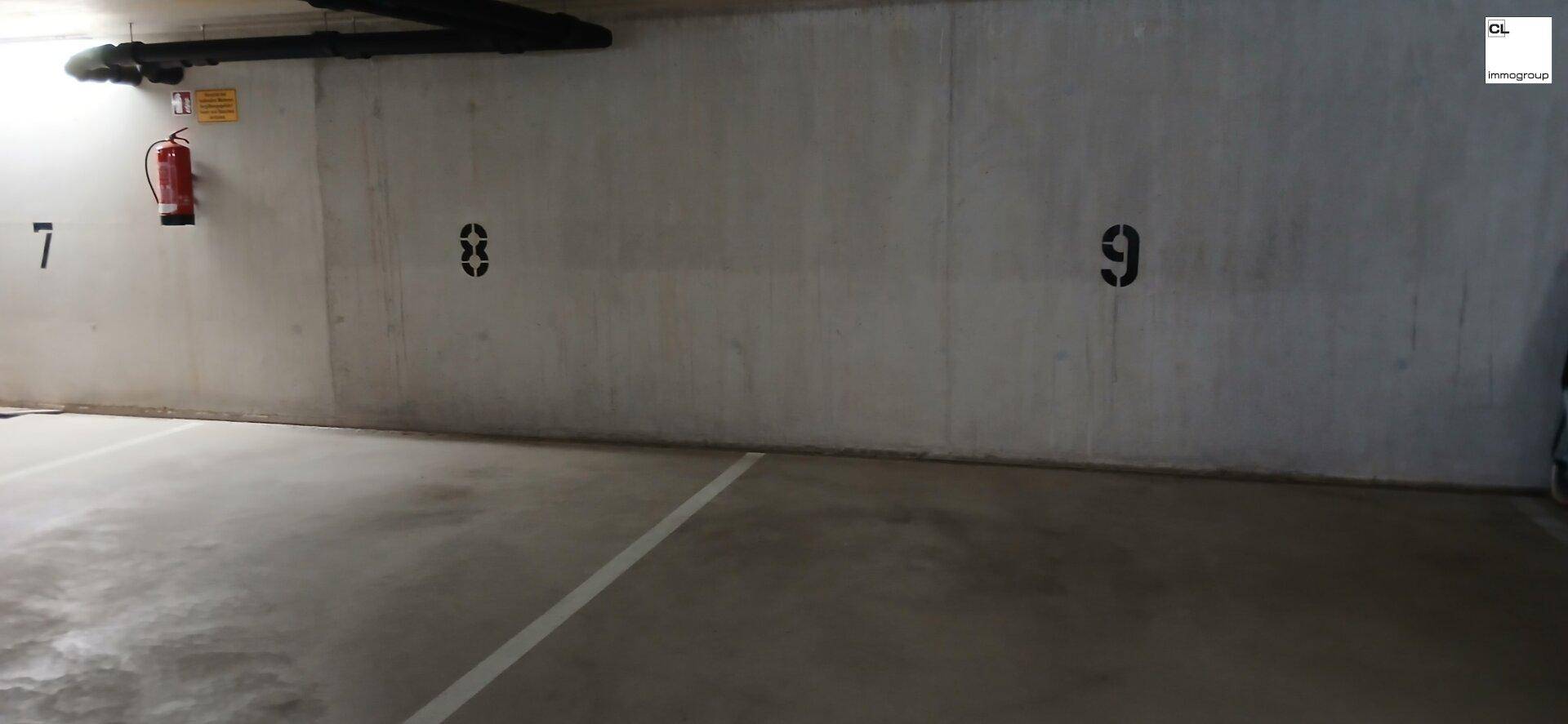 Wandbereich in der Tiefgarage mit nummerierten Stellplätzen und einem sichtbaren Feuerlöscher.