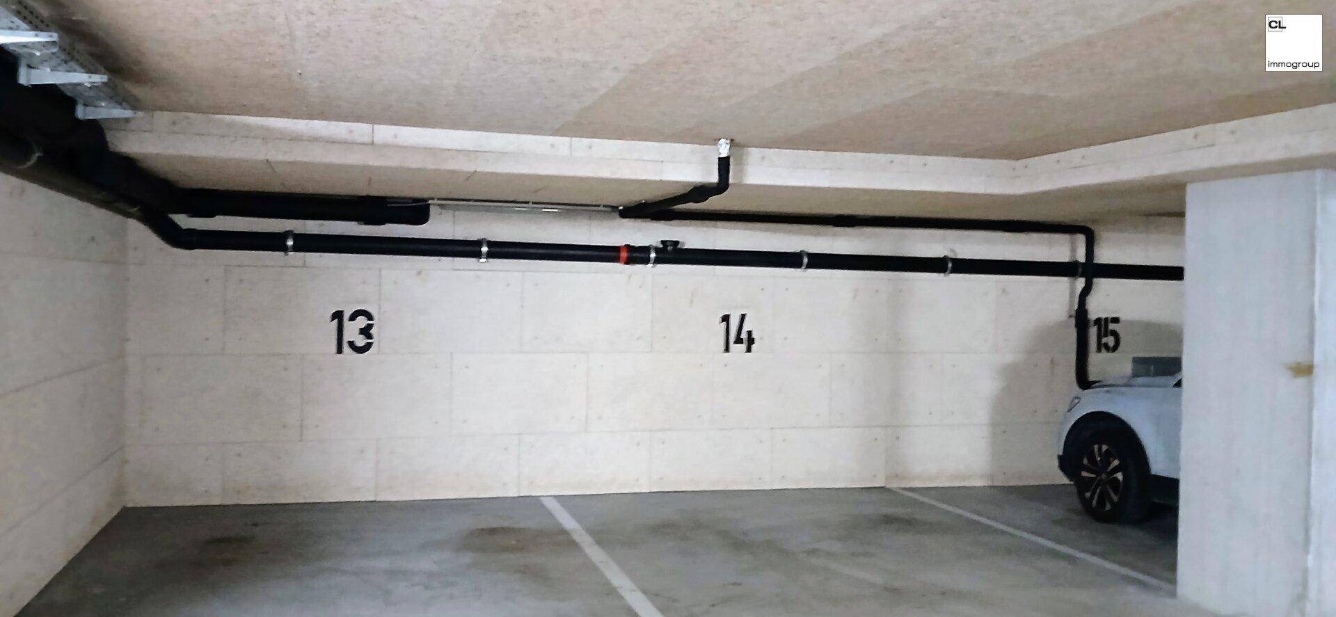 Tiefgarage mit nummerierten Stellplätzen und sichtbaren Versorgungsleitungen an der Decke.