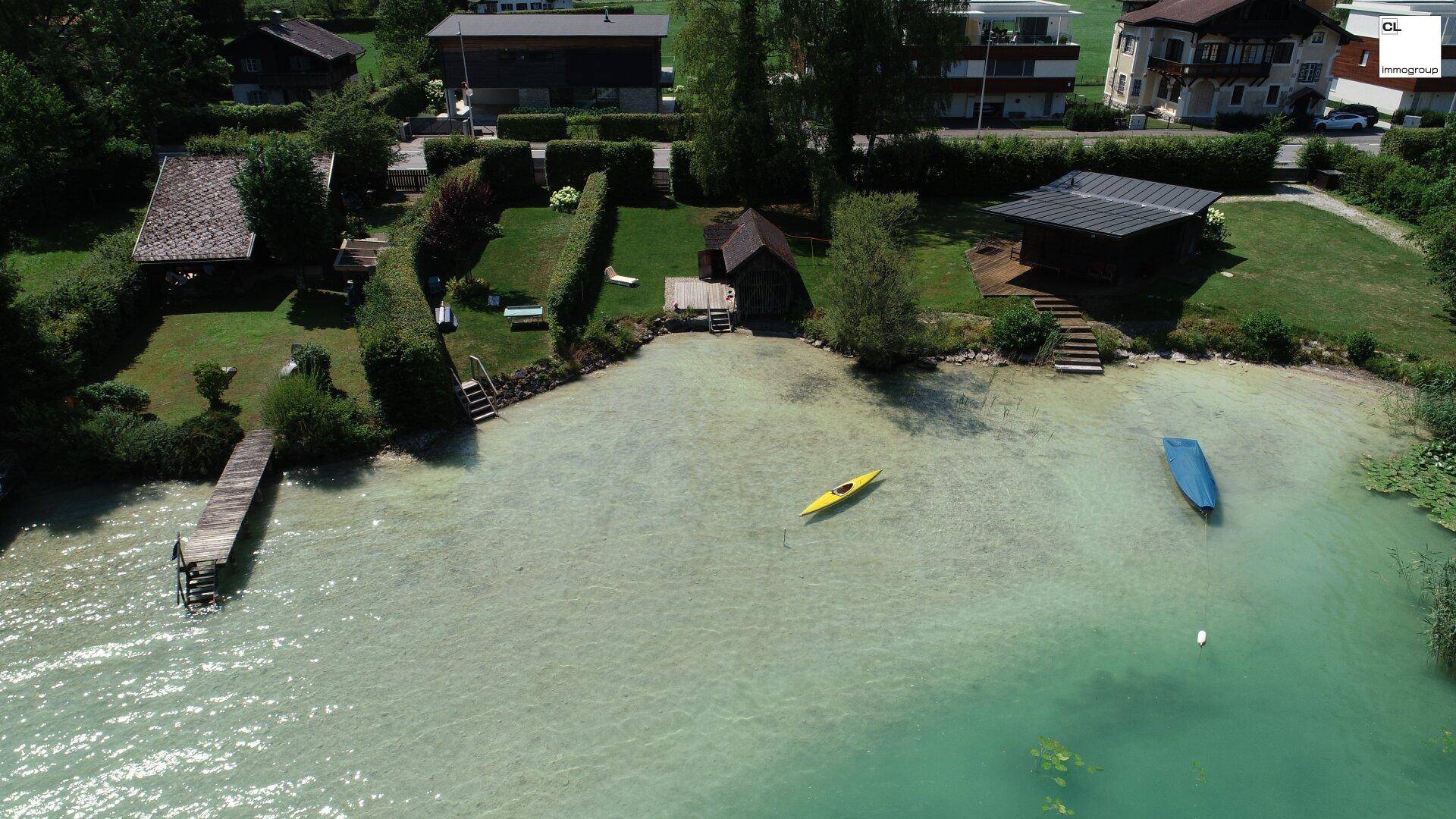 Luftaufnahme eines Seegrundstücks mit privatem Steg, Bootshaus und weitläufiger Rasenfläche am Ufer.