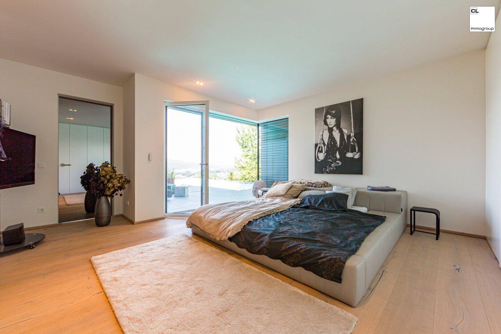 Helles Schlafzimmer mit Holzboden und großen Fenstern, die den Zugang zu einer privaten Terrasse ermöglichen.