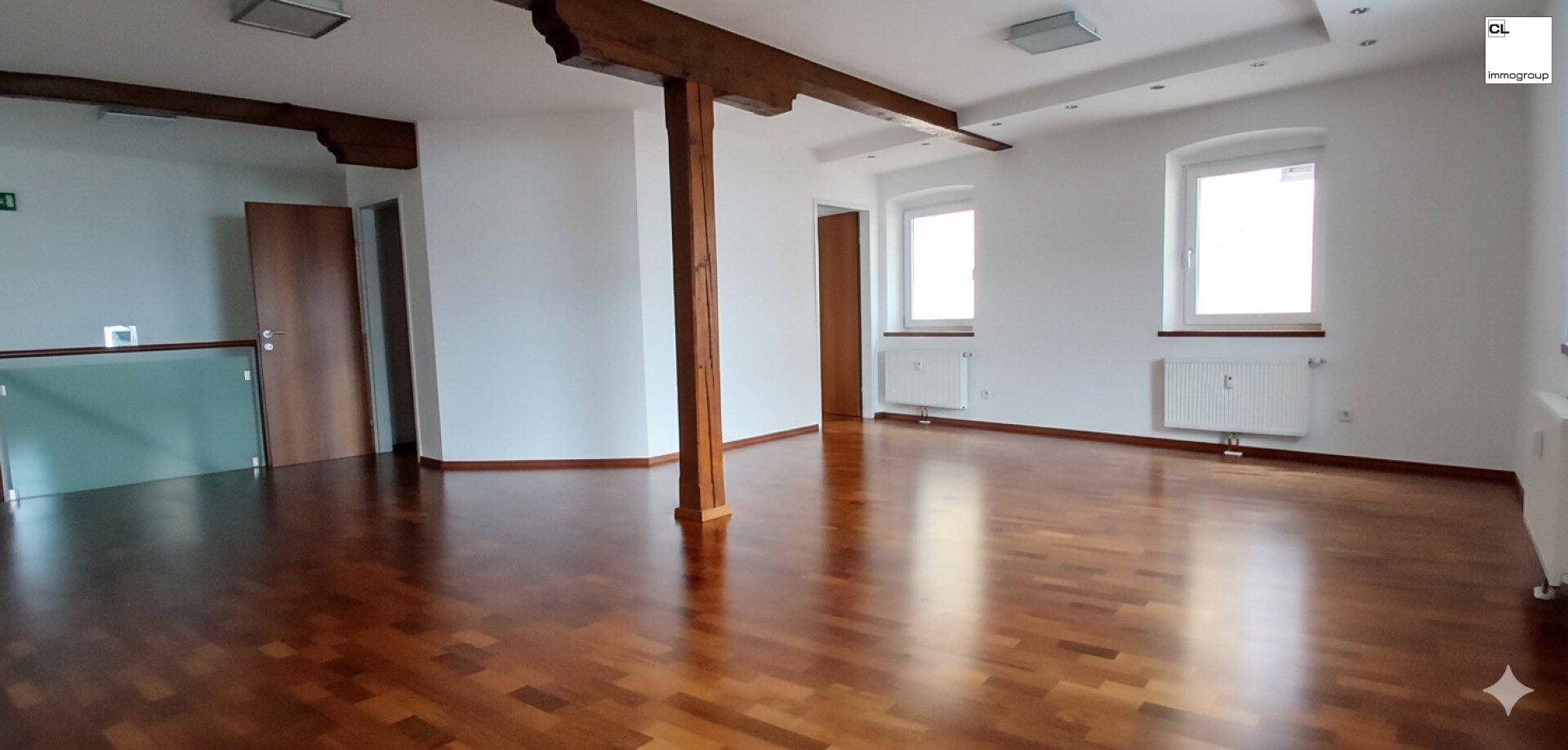 Geräumiger Innenraum mit Holzbalken, Parkettboden und großen Fenstern, ideal für gewerbliche Nutzung.