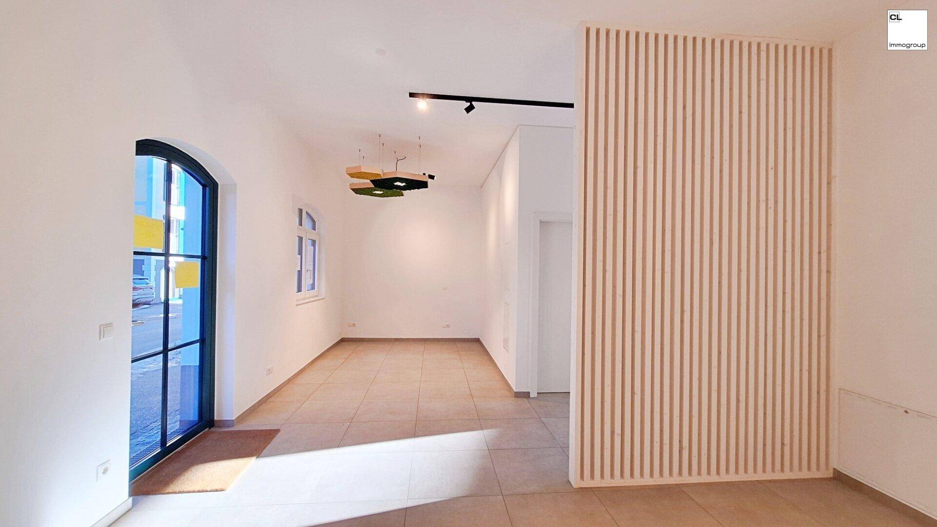 Heller, leerer Raum mit Fliesenboden, Holzwandverkleidung und modernen Deckenleuchten.